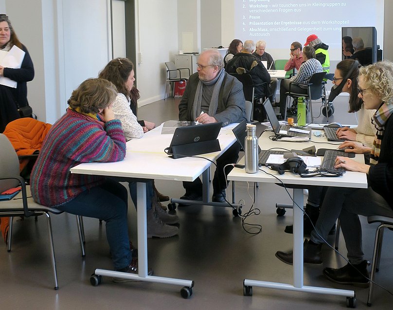 Blick durch den Veranstaltungsraum, drei Tische mit Menschen, die sich jeweils in ihrer Gruppe unterhalten