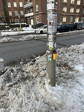 Mit Schneematsch bedeckter Gehweg am Straßenübergang um einen Ampelmast herum.