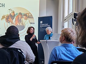 Lilja Häfele-Stephan und Hela Michalski stehen an einem Rednerpult und sind im Gespräch.