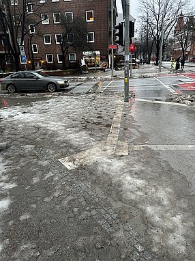 Bodenindikatoren an einer Straßenkreuzung, die mit Eis und Schneematsch bedeckt sind.